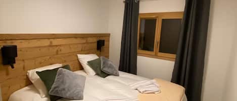 Una cama individual con cabecera de madera, una mesita de noche y una ventana con cortinas.