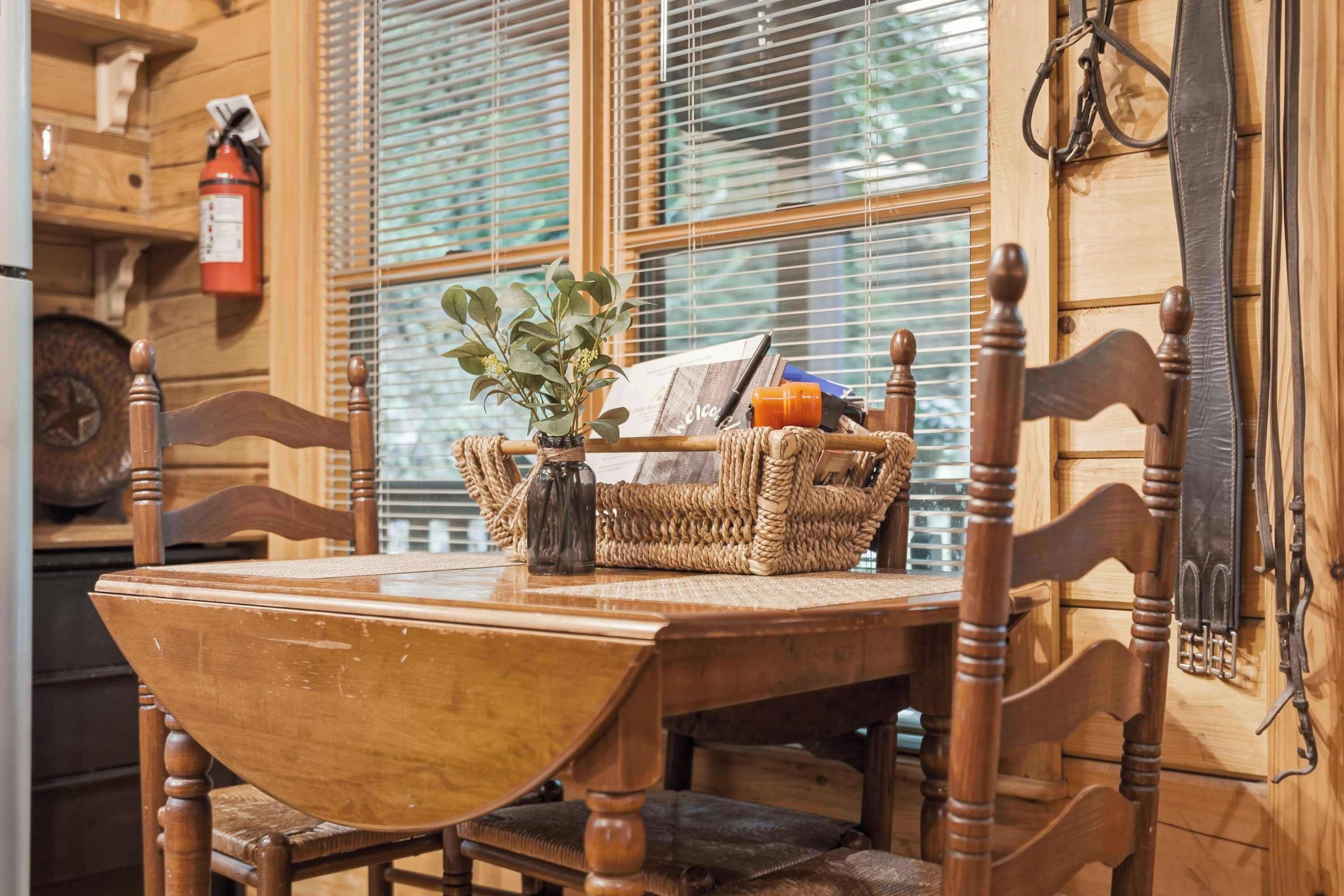 Una mesa de comedor de madera con una cesta tejida que contiene una planta y un libro, frente a una ventana con persianas.