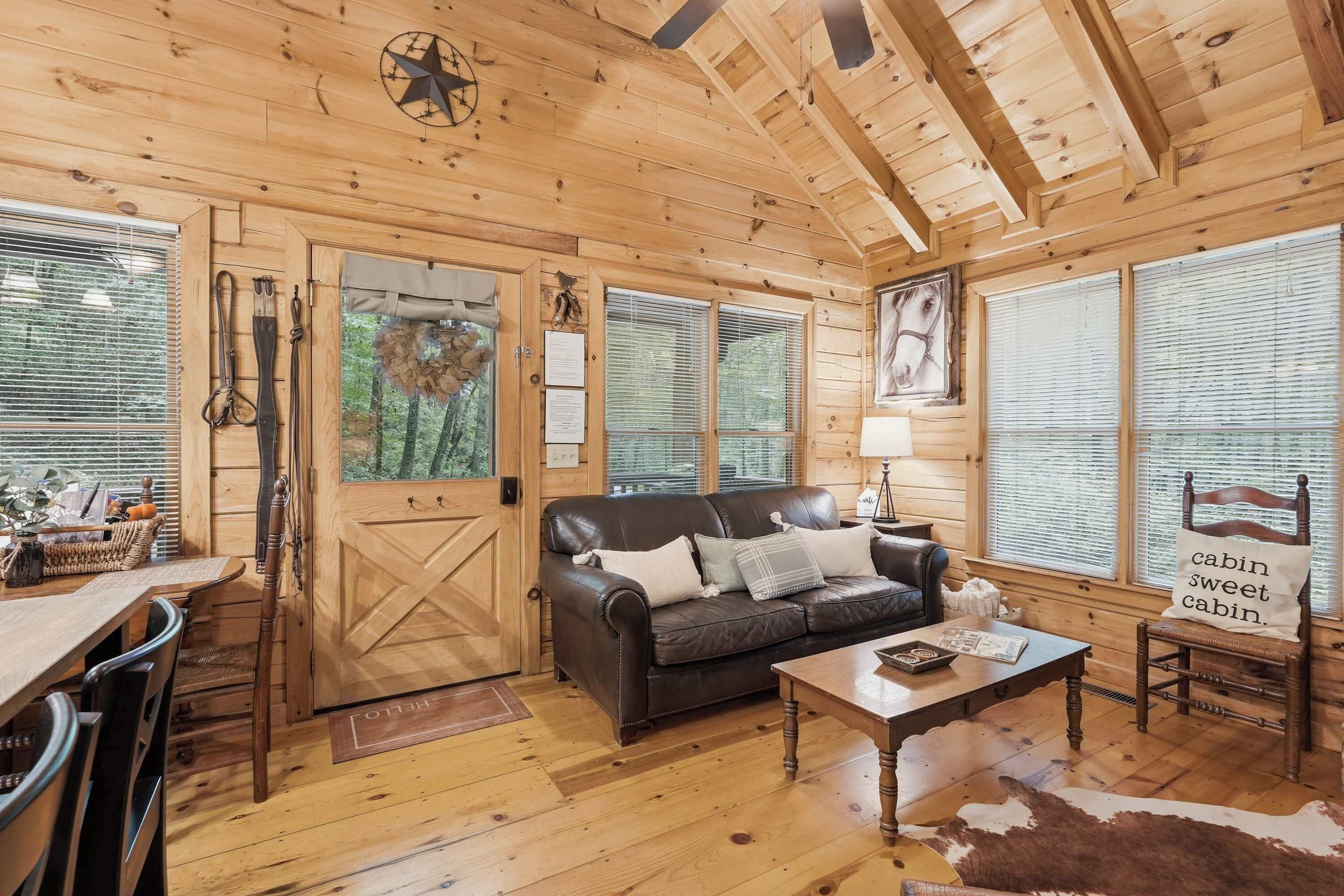 A cabin interior with a wooden floor, a leather sofa, a dining table, and a cowhide rug.