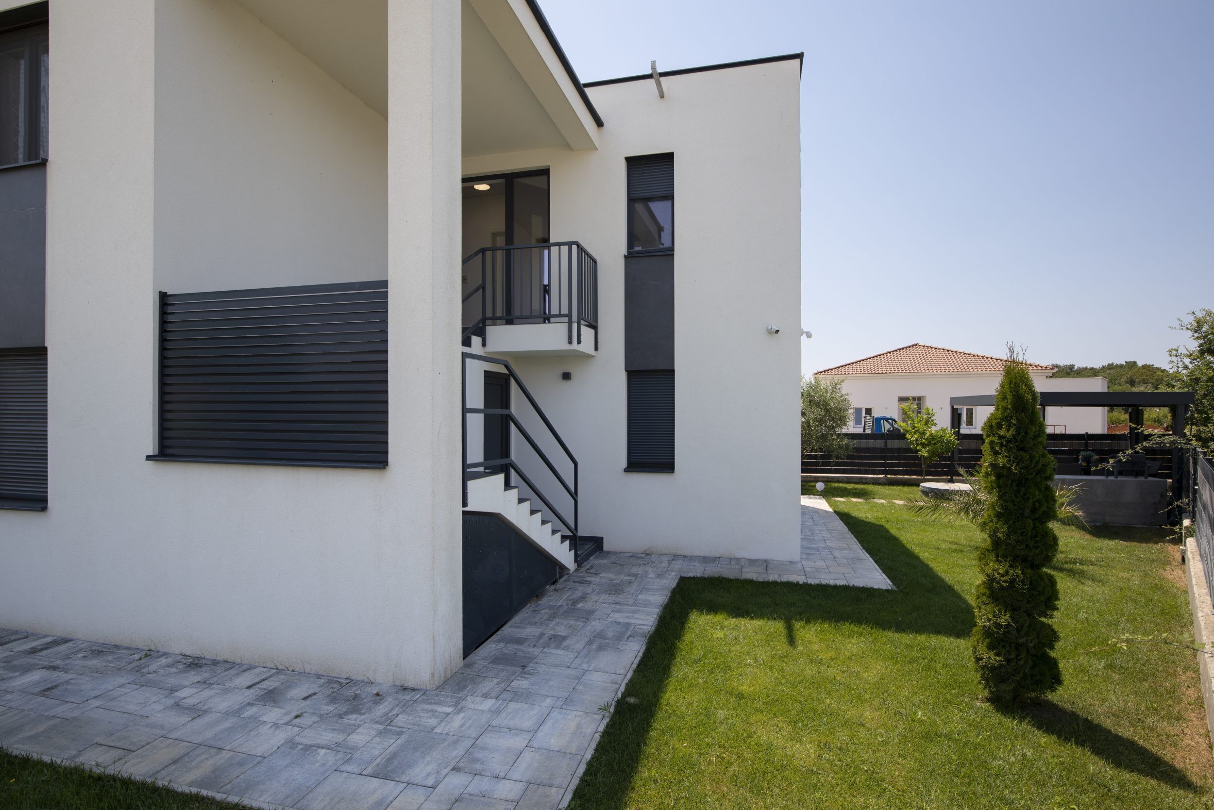 A modern two-story building with a flat roof, a balcony, and a small garden area.