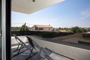 Varanda com estrutura metálica e porta de vidro, com vista para uma área residencial com casas e céu claro.