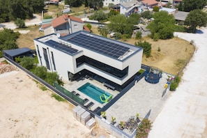 Une maison moderne à deux étages, dotée d’une piscine, de panneaux solaires et d’un trampoline.