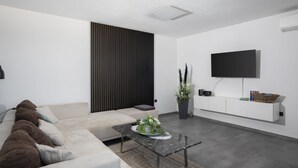 A modern living room with a sofa, a coffee table, a TV mounted on the wall, and a decorative plant. - Apartment Dorota with private Pool near Fažana (Pula)
