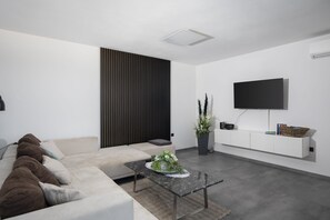 Ein modernes Wohnzimmer mit einer Couch, einem Couchtisch, einem an der Wand befestigten Fernseher und einer Zimmerpflanze.
