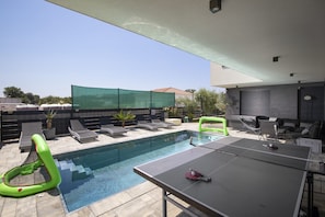 Un espace extérieur avec une piscine, des chaises longues, une table et une table de ping-pong.
