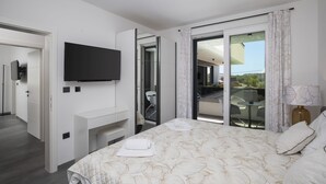 A modern hotel room with a flat-screen TV, a bed with a patterned duvet, a balcony with a table and chairs, and a sliding glass door leading to the balcony. - Apartment Dorota with private Pool near Fažana (Pula)