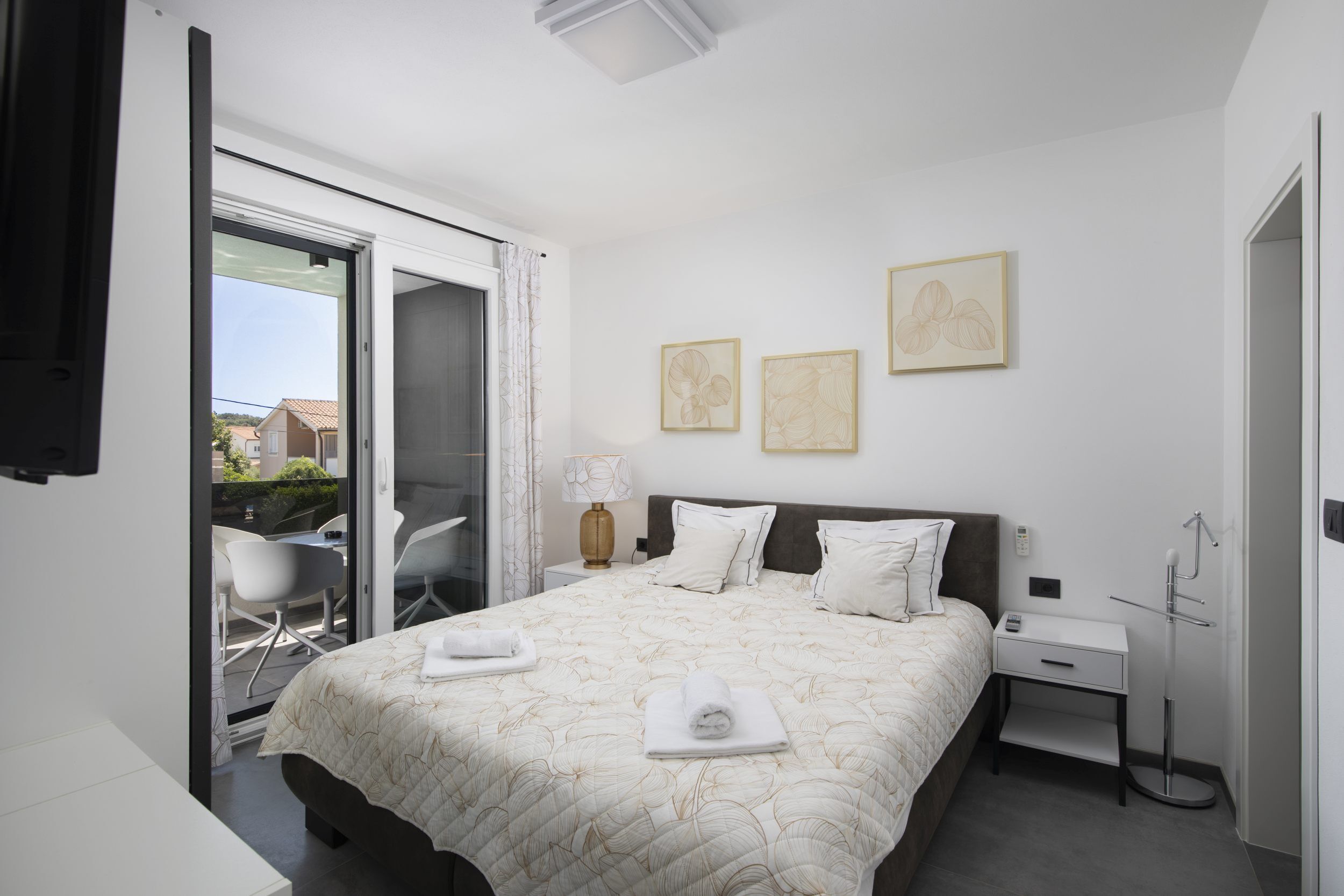 A hotel room with a bed, a bedside table, a lamp, a chair, and a view of the outside.