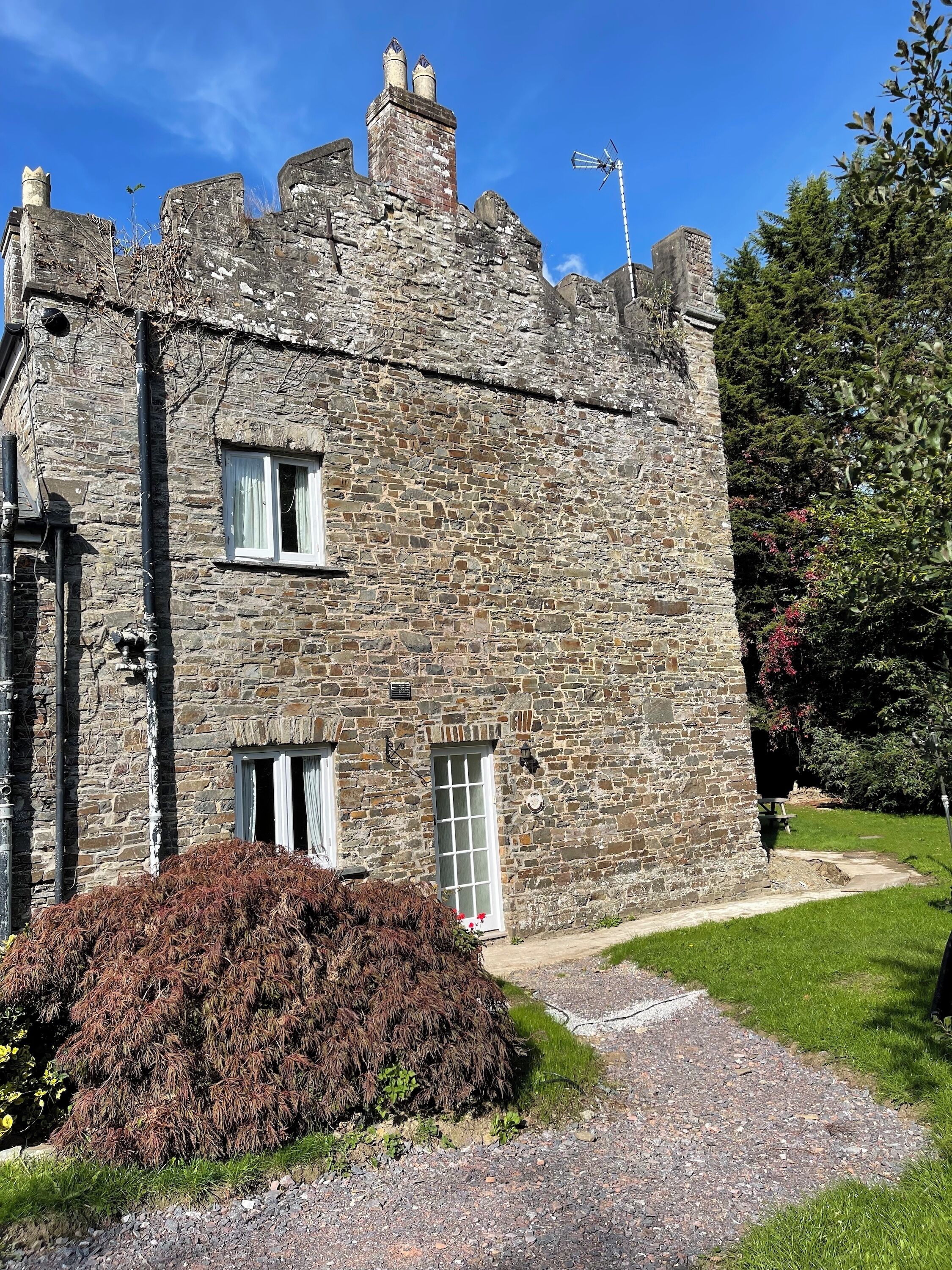 A stone building with multiple chimneys, a small garden, and a clear sky.