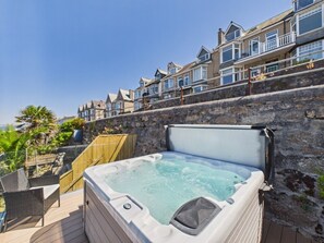 A hot tub on a wooden deck with stone walls and a view of a row of houses. - Coastal Charm | 4BR House | near St Ives Harbour (St Ives)