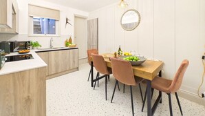 A modern kitchen with a dining area, featuring a wooden table, chairs, and a pendant light. - Coastal Charm | 4BR House | near St Ives Harbour (St Ives)