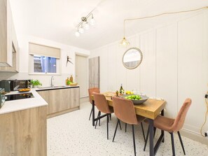 A modern kitchen with a dining area, featuring a wooden table, chairs, and a pendant light. - Coastal Charm | 4BR House | near St Ives Harbour (St Ives)
