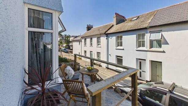 A balcony with a wooden table and chairs, overlooking a street with buildings. - Coastal Charm | 4BR House | near St Ives Harbour (St Ives)