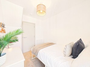 Une chambre à coucher avec un lit, une table de chevet, une lampe et une plante en pot.