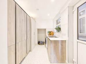 Ein schmaler Flur mit einer Küchenzeile rechts, inklusive Spüle, kleiner Arbeitsplatte und Fenster.