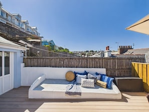 Eine Dachterrasse mit einer weißen Sitzgruppe mit Polstern, einem Holzzaun und freiem Blick auf die umliegende Nachbarschaft.