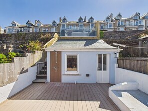 A small, enclosed outdoor area with a wooden deck, a small window, and a door, surrounded by a stone wall and a wooden fence. - Coastal Charm | 4BR House | near St Ives Harbour (St Ives)