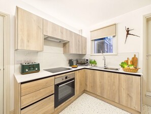 A modern kitchen with wooden cabinets, a built-in oven, a microwave, and a toaster. - Coastal Charm | 4BR House | near St Ives Harbour (St Ives)