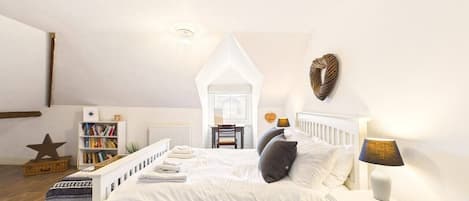 Un dormitorio con cama blanca, mesita de noche y lámpara. Hay una estantería y una decoración con forma de estrella en el suelo.