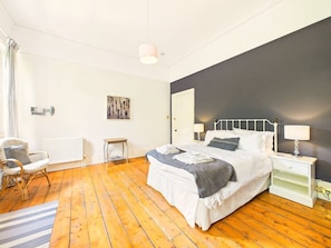 A bedroom with a bed, bedside tables, a chair, a radiator, and a painting on the wall. - Luxury Retreat | Hot-tub | Cinema Room | Sleeps 18 (Gloucestershire)