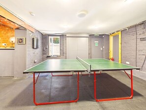 Een kamer met twee pingpongtafels, een bakstenen muur en een deur op de achtergrond.