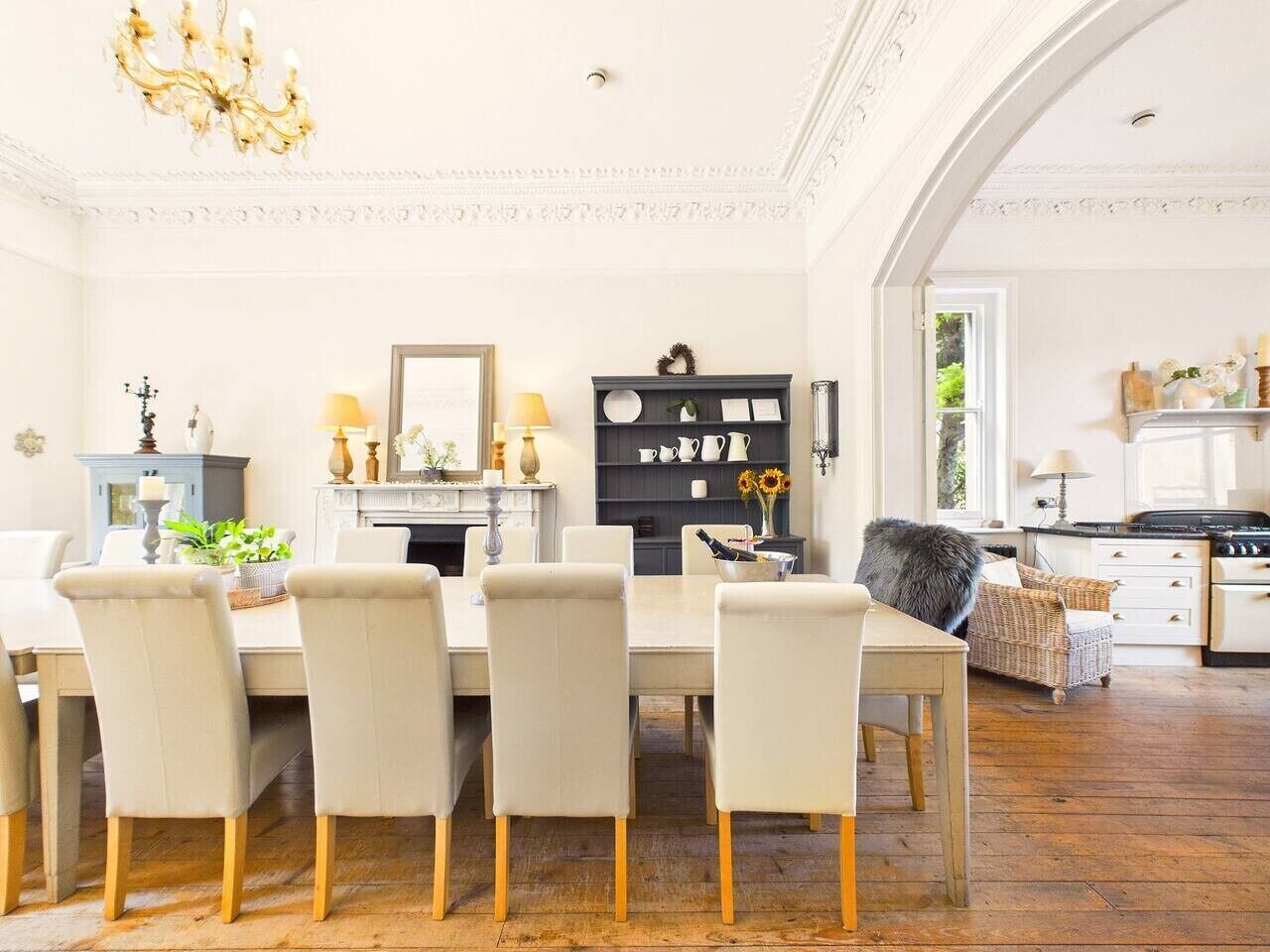 A dining area with a table and chairs, a chandelier, a fireplace, and a kitchen in the background.