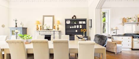A dining area with a table and chairs, a chandelier, a fireplace, and a kitchen in the background.