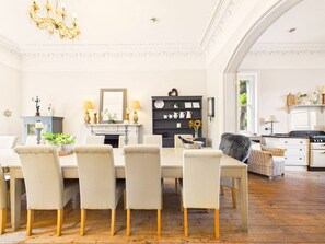 Ein Essbereich mit Tisch und Stühlen, einer Chandelüster, einem Kamin und einer Küche im Hintergrund.