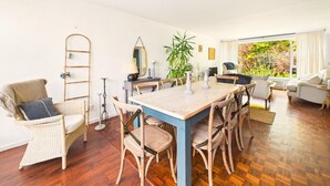 Amplia sala de estar con una mesa de comedor de madera, sillas de mimbre, una escalera y un ventanal con vistas a zonas verdes.