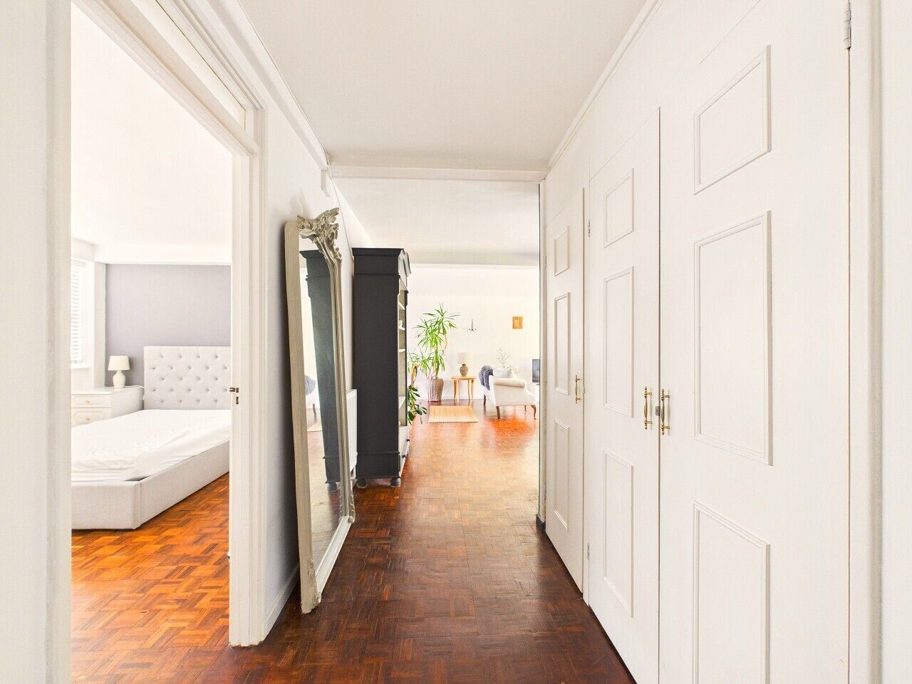 A hallway with a bed, a mirror, and a door leading to another room.