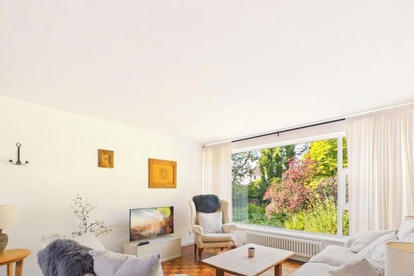 The main sitting room stretches out in soft creams and warm parquet, with a picture window pulling the garden`s colour right into the room.