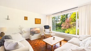 Una sala de estar moderna con un conjunto de sofá, una mesa de centro, un televisor y un ventanal con vistas a zonas verdes.