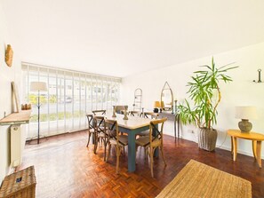 A dining area with a table and chairs, a large window with blinds, a potted plant, and a lamp on a side table.