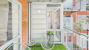 Un balcon avec une petite table et deux chaises, un mur en briques et une vue sur les immeubles voisins.