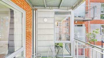 A balcony with a small table and two chairs, a brick wall, and a view of neighboring buildings.