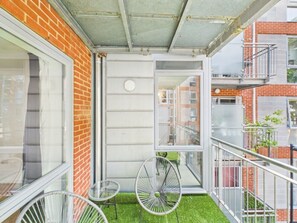 Ein Balkon mit einem kleinen Tisch und zwei Stühlen, eine Ziegelwand und Blick auf angrenzende Gebäude.