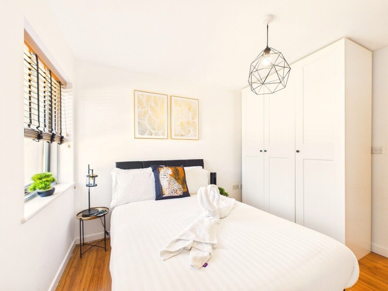 Une chambre à coucher comprenant un lit, une table de chevet, une armoire et une fenêtre avec des stores.