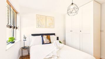A bedroom with a bed, a bedside table, a wardrobe, and a window with blinds.