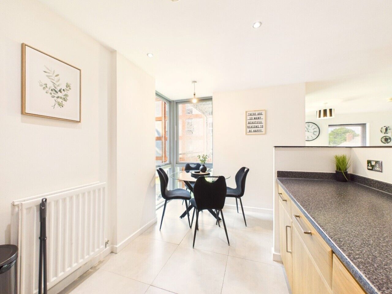 A modern kitchen with a dining area, white walls, and a window providing natural light.