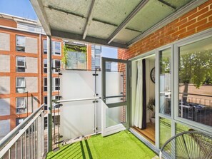 Ein Balkon mit Glastür, Metallgeländer und Blick auf ein Backsteingebäude.