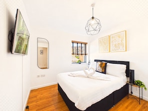 A modern bedroom with a bed, a TV mounted on the wall, a window with blinds, and framed artwork on the wall. - Stylish Central Apartment | Balcony | Free Parking (Greater London)