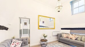 A living room with a grey sofa, a round side table with a vase, a large mirror, and a patterned rug. - High Street | Boutique 2 Bedroom | Wi-Fi (Essex)