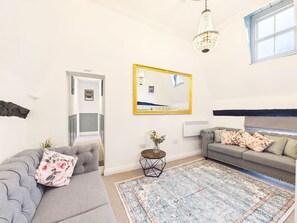 Una sala de estar con un sofá gris, una mesita redonda con un florero, un espejo grande y una alfombra estampada.