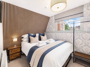 A bedroom with a bed, bedside table, lamp, and a window with a view.