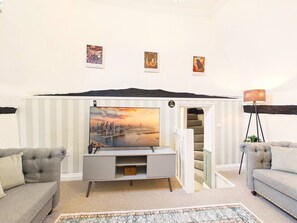 A living room with a flat-screen TV, grey sofas, a patterned rug, and a staircase leading to an upper level.