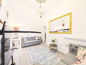 A living room with a grey sofa, a round coffee table, a chandelier, and a large mirror with a yellow frame.