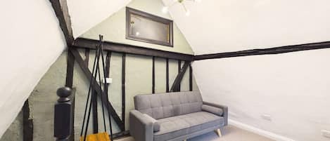 Una habitación con un sofá gris, techo con vigas a la vista en blanco y negro, y una lámpara moderna.