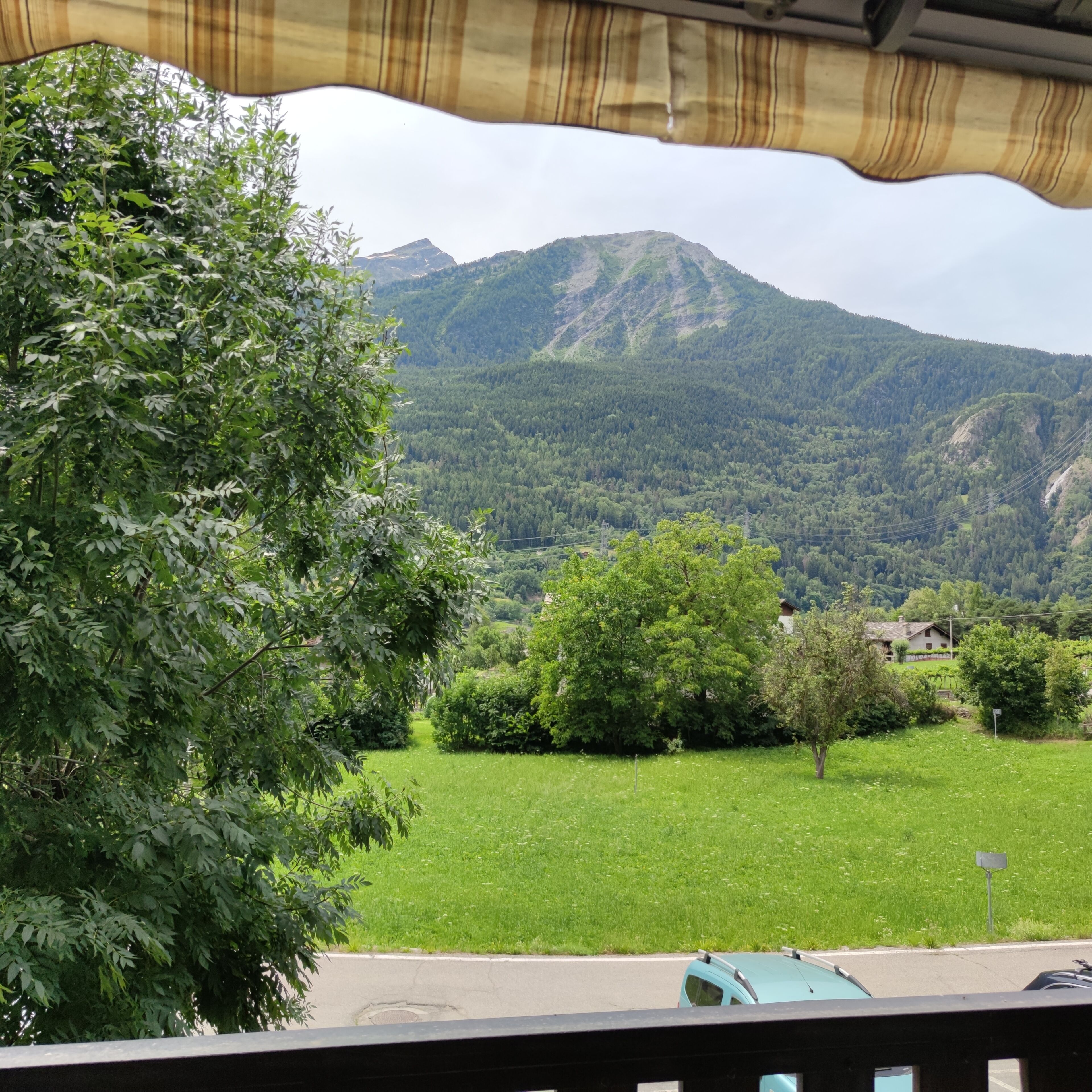 Une vue sur un paysage montagneux, avec un champ verdoyant et des arbres au premier plan.