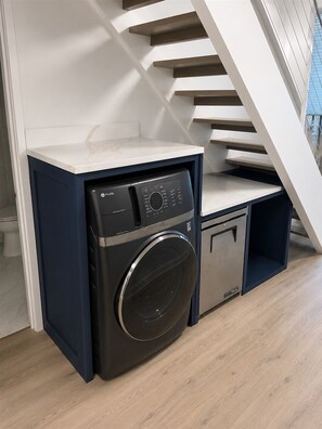 A compact laundry area with a washing machine and a dryer, located in a room with wooden flooring and a white staircase. - Beach Villa 2126: Rare 2-Story Gulf-Front Gem – Panoramic Views & Brand New Loft (Captiva)