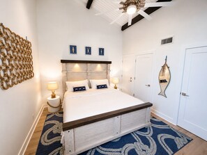A bedroom with a bed, bedside lamps, a ceiling fan, a wall-mounted mirror, and a decorative wall piece. - Beach Villa 2126: Rare 2-Story Gulf-Front Gem – Panoramic Views & Brand New Loft (Captiva)