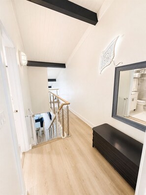 Un intérieur moderne avec un plancher en bois, un escalier, un banc noir et un grand miroir.